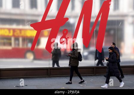 Les gens passent devant un panneau de grande taille pour la marque de vêtements et de vêtements de grande rue H&M à l'extérieur de leur magasin phare, à l'angle d'Oxford Street et de Regent Street. Le 30th mars 2023 à Londres, Royaume-Uni. Banque D'Images