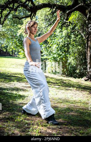 une femme pratiquant le tai chi dans un parc transmet un sentiment de tranquillité et d'harmonie avec la nature. Banque D'Images