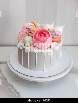 Beau et élégant gâteau gris décoré avec du chocolat blanc fondu, des macarons, une fleur de pivoine rose, des gâteaux et des bonbons sur le cakestan de marbre Banque D'Images