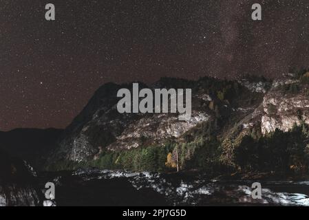 Rive en pierre de la rivière Katun dans l'ombre la nuit par une montagne éclairée par la lumière sous les étoiles avec la voie lactée dans l'Altaï en Sibérie. Banque D'Images