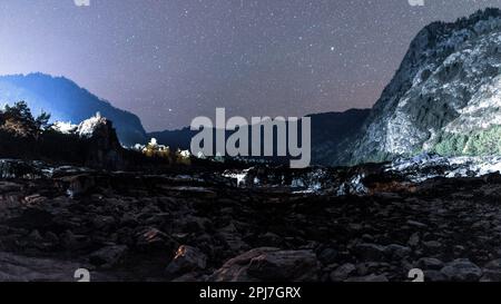 La rive en pierre de la rivière Katun à l'ombre la nuit près des montagnes illuminée par la lumière des maisons de repos sous les étoiles de l'Altaï Banque D'Images