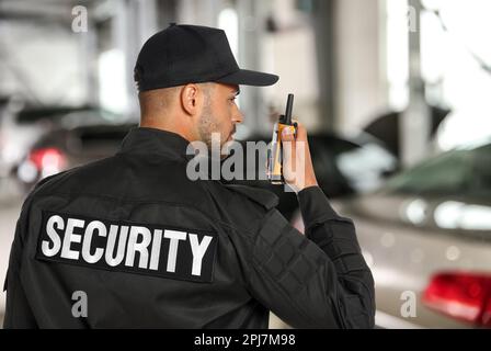 Un agent de sécurité mâle portant un uniforme utilisant un émetteur radio portable au stationnement Banque D'Images