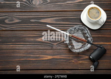 Cendrier avec porte-cigarettes long, briquet et tasse de café sur table en bois, plat. Espace pour le texte Banque D'Images