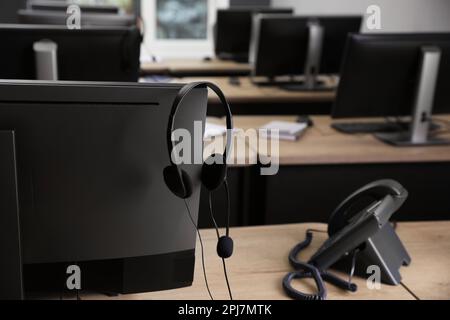 Téléphone fixe près d'un ordinateur moderne avec casque sur un bureau en bois à l'intérieur. Service d'assistance téléphonique Banque D'Images