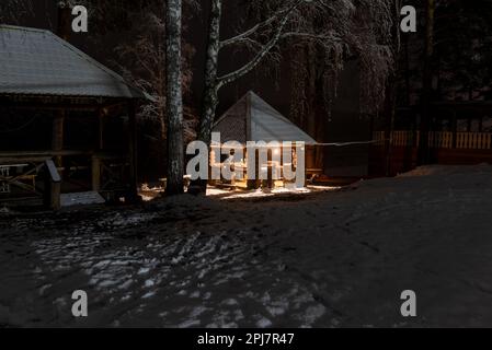 Maison de vacances avec deux femmes se reposant dans la neige sous les oiseaux la nuit avec un feu de barbecue dans l'Altaï Banque D'Images