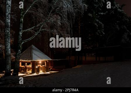 Maison de vacances avec deux femmes se reposant dans la neige sous les birches la nuit avec un feu de brazier en Altaï en Russie. Banque D'Images