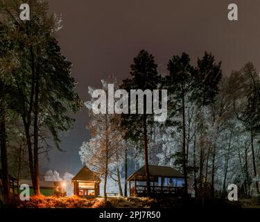 Maison de vacances sur la rive avec deux femmes se reposant dans la neige sous les birches la nuit avec un feu de brasier à Altai en Sibérie dans l'obscurité. Banque D'Images