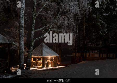 Maison de vacances avec deux femmes se reposant dans la neige sous les birches la nuit avec un feu de brasier à Altai en Russie dans l'obscurité. Banque D'Images