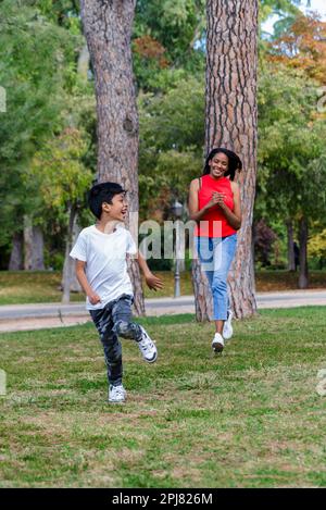 Joyeux garçon ayant du plaisir à courir avec sa mère à l'extérieur dans un parc. Banque D'Images