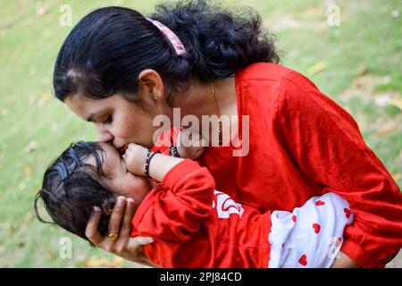 Maman aimante portant son bébé au parc de la société. Portrait lumineux d'une mère heureuse tenant l'enfant dans ses mains. Mère embrassant son petit fils de 9 mois. Banque D'Images