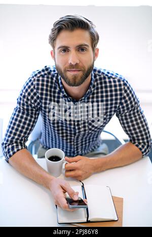 Beaucoup de travail à faire. Portrait d'un homme d'affaires utilisant son téléphone portable et buvant du café à son bureau. Banque D'Images