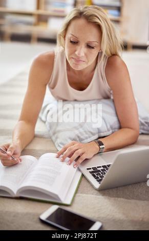 Il est temps de se détendre. une belle femme mûre couché sur le sol de son salon faisant quelques recherches. Banque D'Images