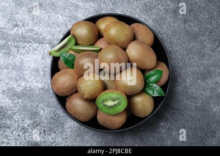 Kiwis frais mûrs dans un bol sur une table grise, vue de dessus Banque D'Images