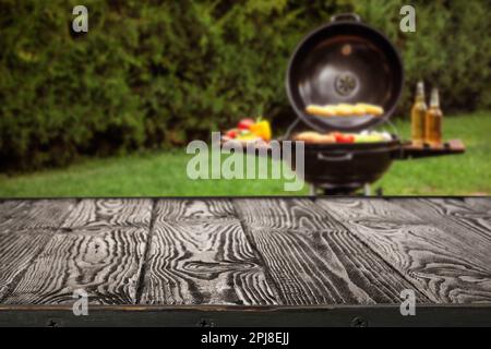 Table en bois noir vide et vue floue de la nourriture savoureuse sur le barbecue moderne en plein air Banque D'Images