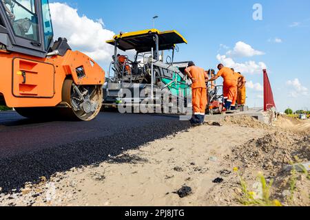 L'asphalte chaud se répand avec le rouleau à vapeur. La machine de pose de l'asphalte est l'épandage de la couche de tarmac chaud sur un sol préparé quelques ouvriers travaillent ar Banque D'Images