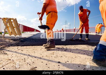Peu de travailleurs utilisent des pelles pour niveler, mettre en place une couche de tarmac frais à la bonne mesure, verser de l'asphalte chaud. Banque D'Images