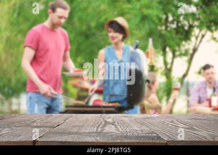 Table en bois vide et vue floue des personnes ayant barbecue avec grill moderne à l'extérieur Banque D'Images