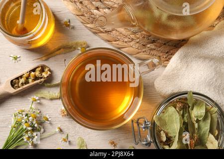 Thé fraîchement infusé, miel et herbes séchées sur une table en bois blanc, plat Banque D'Images