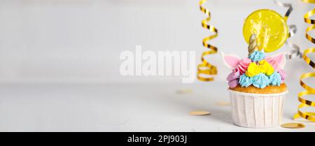 Cupcake mignon de licorne avec une lipop jaune sur une table blanche, espace pour le texte. Bannière Banque D'Images