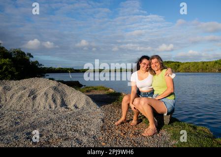 Mère et fille assise au bord de la rivière embrassant. En fin d'après-midi. Rivière en arrière-plan. Banque D'Images