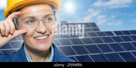 Portrait d'une femme ingénieur en casque et lunettes de protection sur un fond de station d'énergie solaire. Photo de haute qualité Banque D'Images