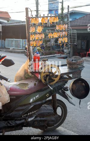 SAMUT PRAKAN, THAÏLANDE, 24 2023 MARS, le calmar sec pressé pendent d'un support monté sur une moto d'un vendeur de rue à la lumière du coucher du soleil, Thaïlande Banque D'Images