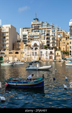 Bateau de pêche et pêcheur dans la baie de Spinola à Saint Julian avec ses nombreux appartements, Malte, Europe Banque D'Images