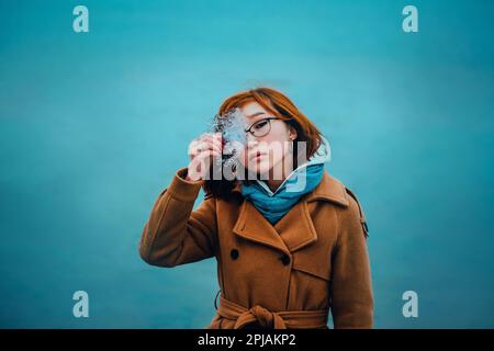 Portrait d'une belle jeune femme asiatique aux cheveux rouges tenant un morceau de glace transparent dans sa main, debout sur le fond d'une mer gelée i Banque D'Images