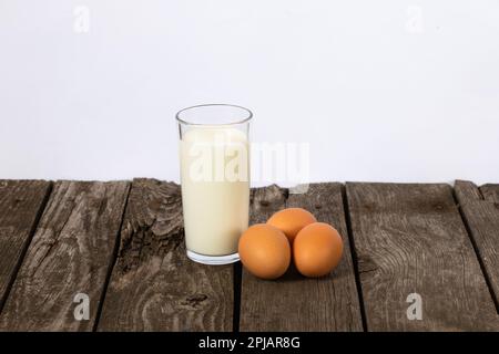 un verre de lait et trois œufs de poulet sur une table Banque D'Images