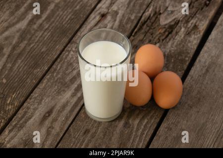 un verre de lait et trois œufs de poulet sur une table Banque D'Images