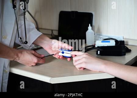 Test d'oxygène pour le covid. Médecin examinant le patient avec un oxymètre de pouls du bout des doigts sur une table en bois, en gros plan. Banque D'Images