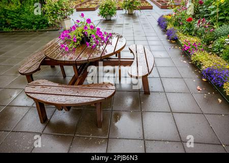 Humide de la table de pluie et des bancs, des chaises dans le jardin avec des gouttes d'eau et avec des fleurs en pot roses sur le dessus. Patio avec carrelage humide. Banque D'Images