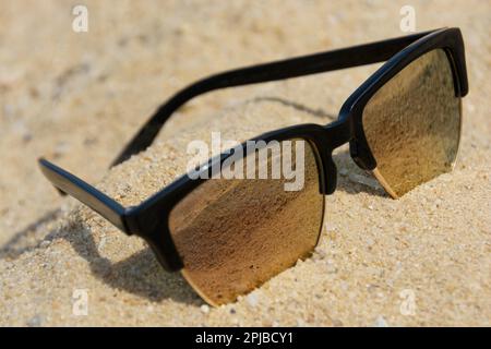 Les lunettes de soleil se trouvent dans le sable. Des lunettes de soleil modernes se trouvent dans le sable Banque D'Images