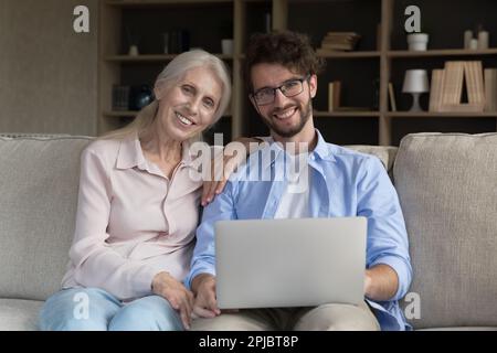 Joyeux et intelligent jeune homme aidant avec l'ordinateur à la mère âgée Banque D'Images