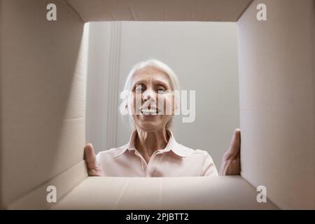 Heureuse joyeuse femme âgée regardant l'appareil photo par boîte en carton Banque D'Images