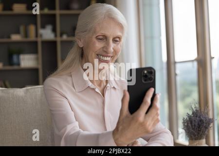 Une vieille grand-mère gaie qui parle à sa famille lors d'un appel vidéo Banque D'Images