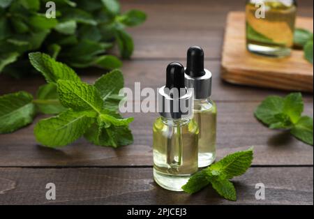 Bouteilles d'huile essentielle et de menthe sur table en bois, gros plan Banque D'Images