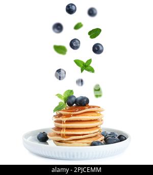 Bleuets frais et feuilles de menthe tombant sur des crêpes empilées sur fond blanc Banque D'Images