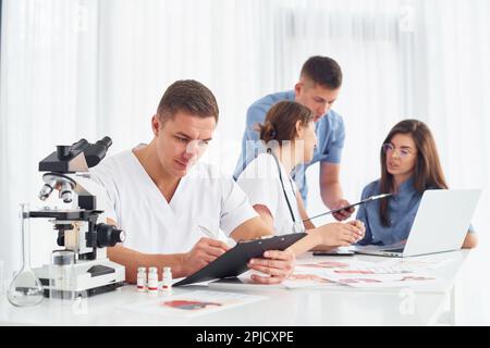 Homme au microscope. Groupe de jeunes médecins travaille ensemble dans le bureau moderne Banque D'Images