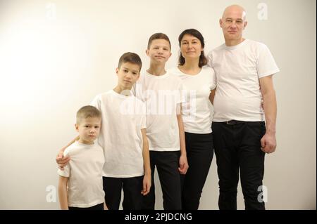 Portrait de la jeune belle famille, du père barbu, de la mère blonde et de leurs petits enfants portant des jeans et des T-shirts blancs debout dans l'ordre de la hiérarchie, en plaçant les mains des têtes les unes des autres Banque D'Images