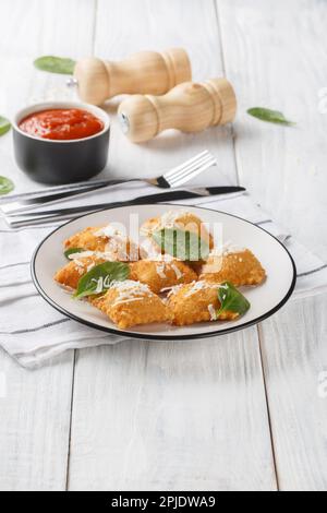 Raviolis frits croustillants aux épinards et au fromage servis avec de la sauce marinara sur une assiette sur une table en bois. Verticale Banque D'Images