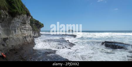 De grandes vagues se brisent sur les rochers de la plage de Muriwai. Bouée de sauvetage orange sur le rocher. Auckland. Banque D'Images