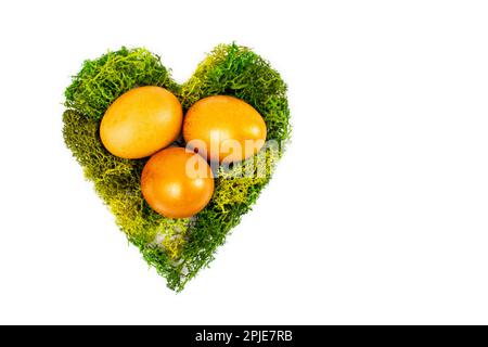 Trois œufs d'or dans un nid en forme de coeur fait de mousse verte isolée sur fond blanc Banque D'Images