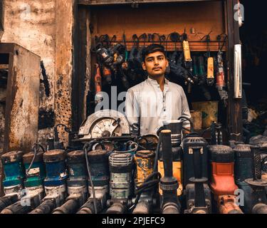 Karachi Pakistan 2019, un garçon assis dans une petite boutique vendant et réparant des machinesi de forage tôt le matin. Banque D'Images