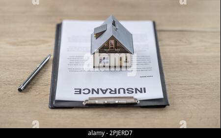 Concept de contrat d'assurance maison avec un modèle de maison au-dessus de la paperasse sur une table à côté d'un stylo. Banque D'Images