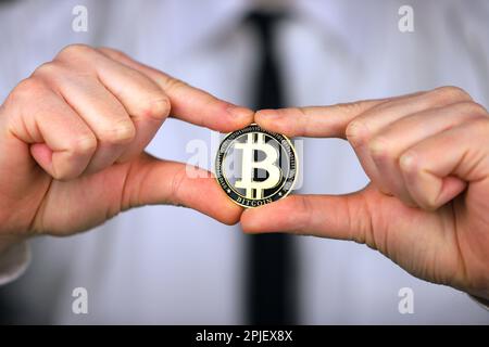 Un homme d'affaires dans une chemise blanche et une cravate noire tient une version physique de bitcoin dans ses mains. Banque D'Images