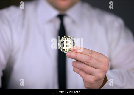Un homme d'affaires dans une chemise blanche et une cravate noire tient une version physique de bitcoin dans ses mains. Banque D'Images