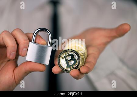 Un homme d'affaires tient un cadenas argenté et une version physique du bitcoin entre ses mains. Interdiction des crypto-monnaies, des règlements, des restrictions ou des sécurs Banque D'Images