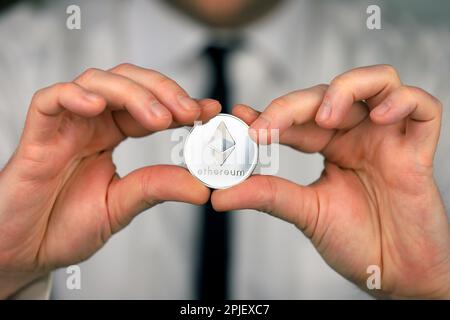 Un homme d'affaires dans une chemise blanche et une cravate noire tient une version physique de l'éthérum dans ses mains. Banque D'Images