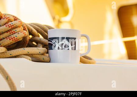 Coupe blanche avec barre dessinée sur le pont d'un yacht blanc, bateau, bateau. Concept de thé café boire tout en voyageant à l'océan de mer. Une tasse parmi les cordes de mer Banque D'Images